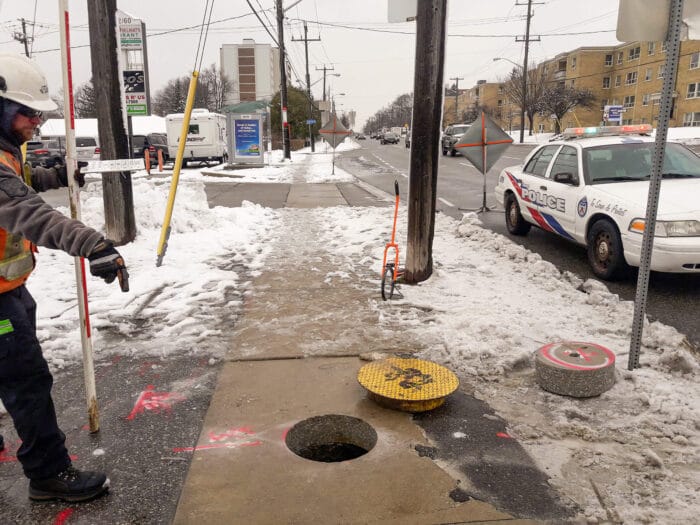 Open test hole on sidewalk with cover to the upper right of it