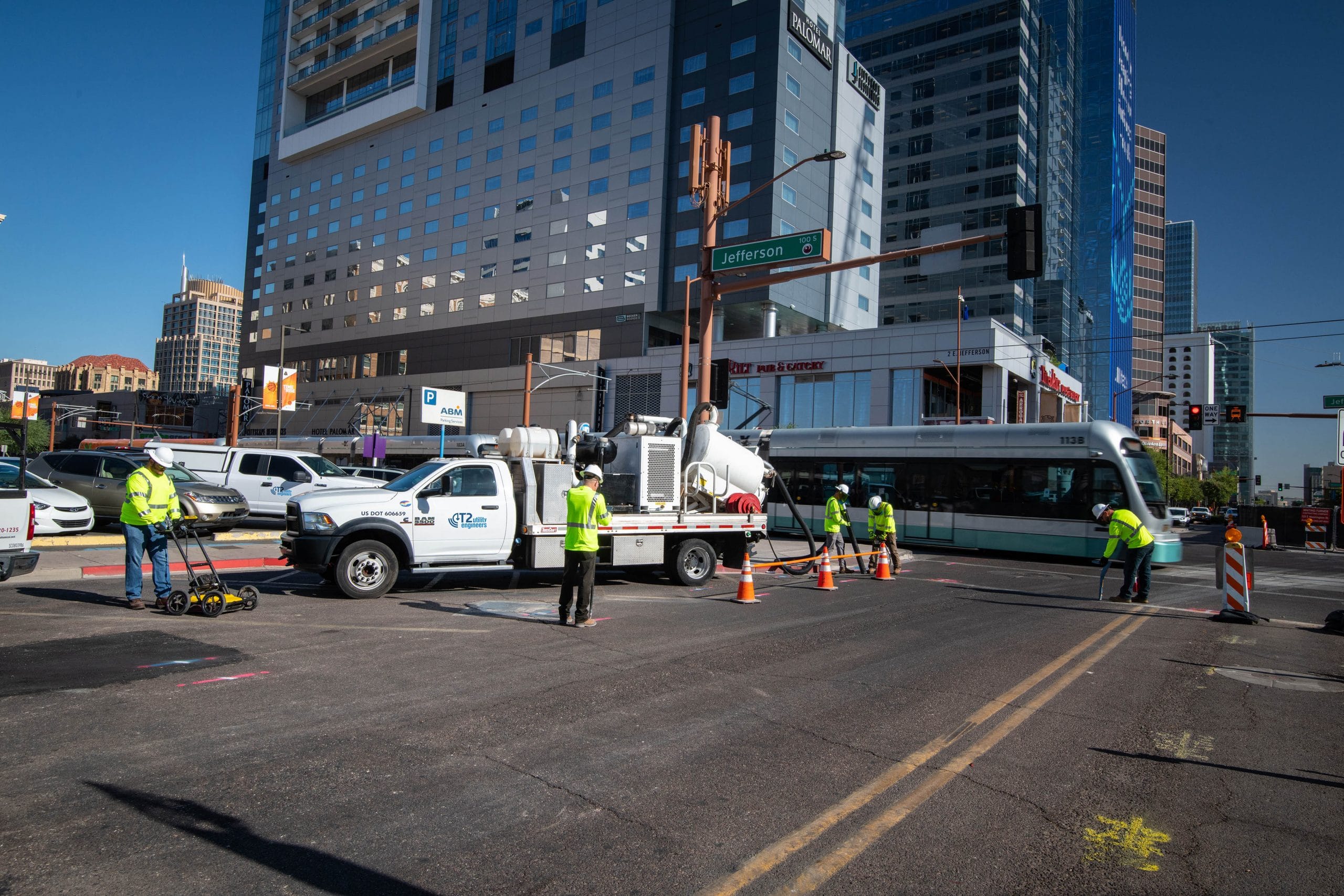 5 travailleurs de terrain en tenue de sécurité menant une enquête sur les services publics le long d'une route urbaine au passage d'un train de banlieue