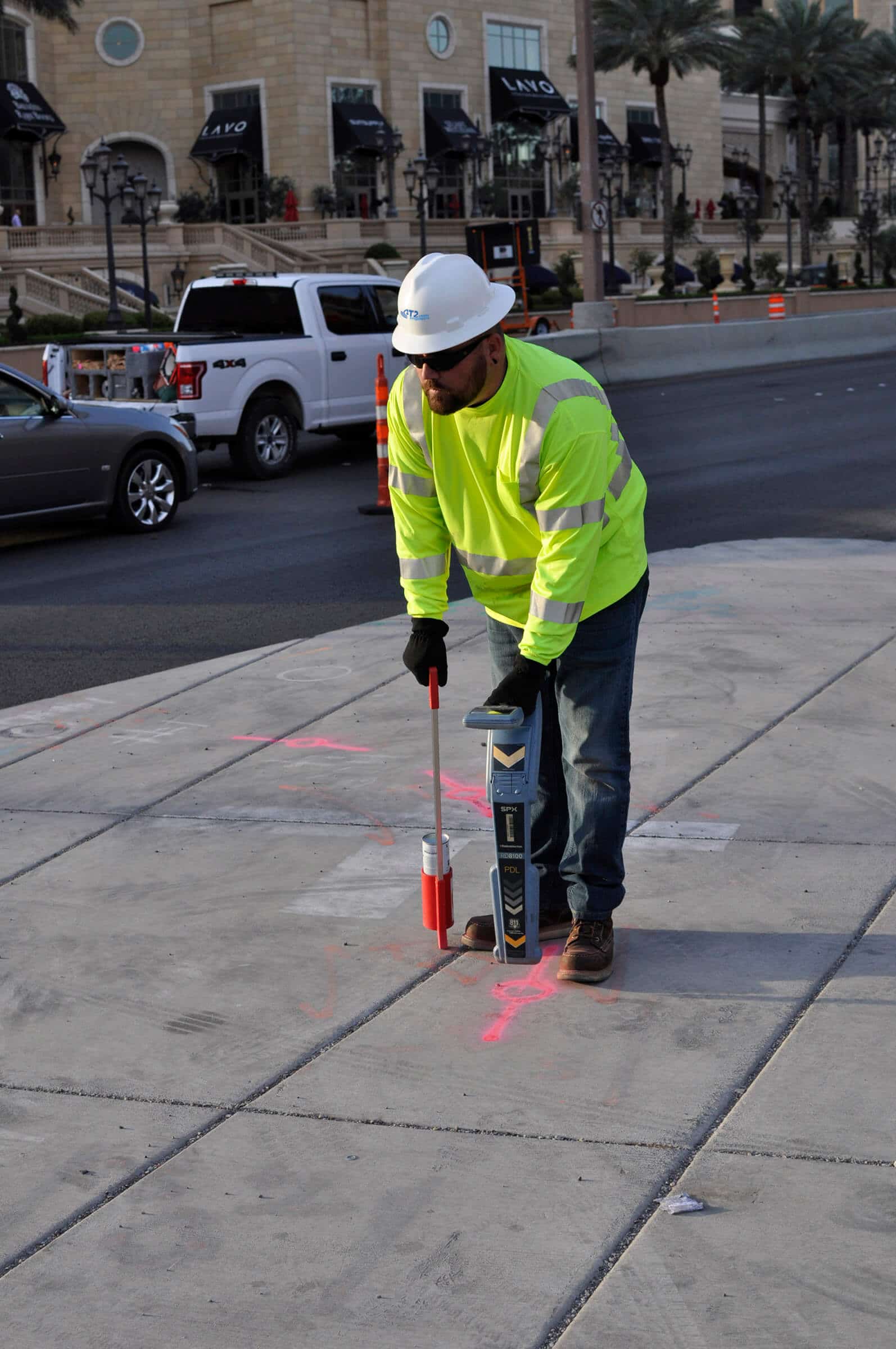 Man wearing T2 Utility Engineers safety clothing using a pipe and cable locator to mark utilities on an urban sidewalk