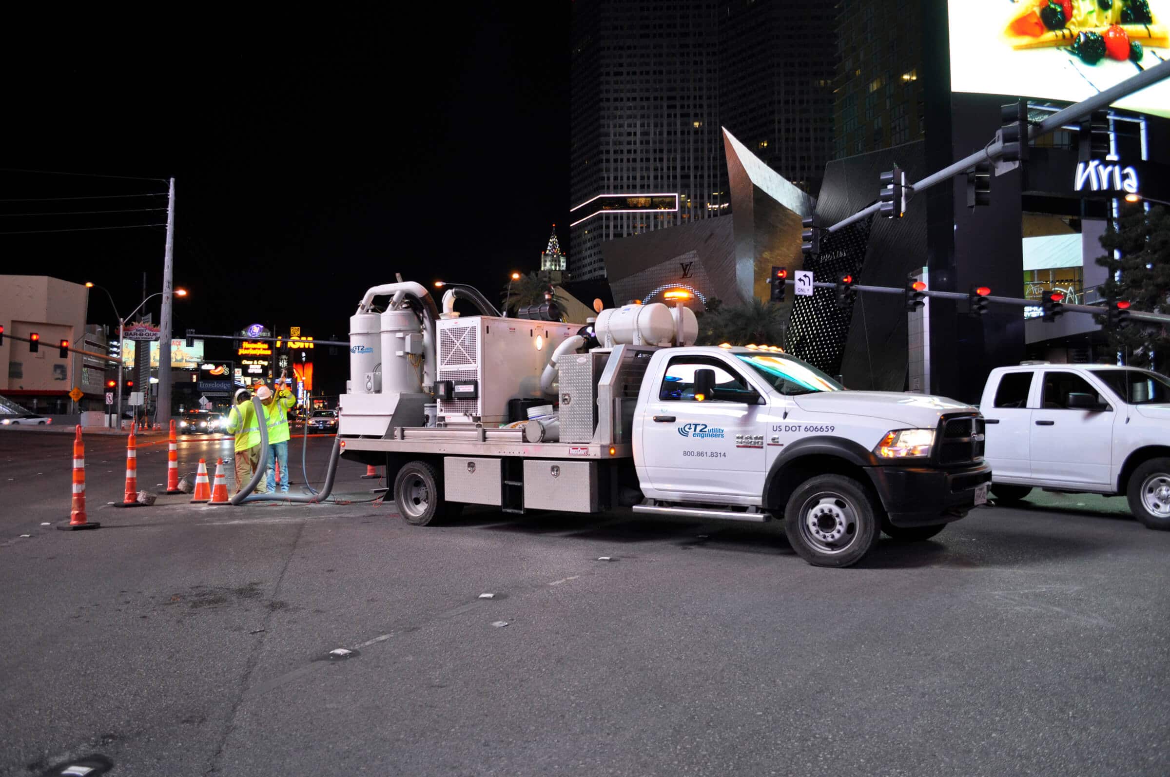 Two workers performing vacuum excavation at night on the Las Vegas strip with vacuum truck in view
