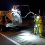 Two T2ue field workers performing a vacuum excavation investigation at night along a highway
